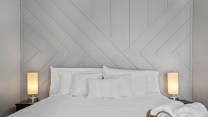 A neatly made bed with white linens, two bedside lamps, and a woven basket with towels.