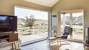 A modern living room with a large TV, a comfortable chair, a sofa, and a view of a desert landscape through large glass doors.