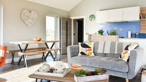 A modern living room with a grey sofa, wooden coffee table, and a dining area with a wooden bench.