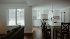 A spacious kitchen with white cabinetry, a large island with bar stools, and pendant lighting. - The Little Green Cottage in the Woods (Glen Arbor)