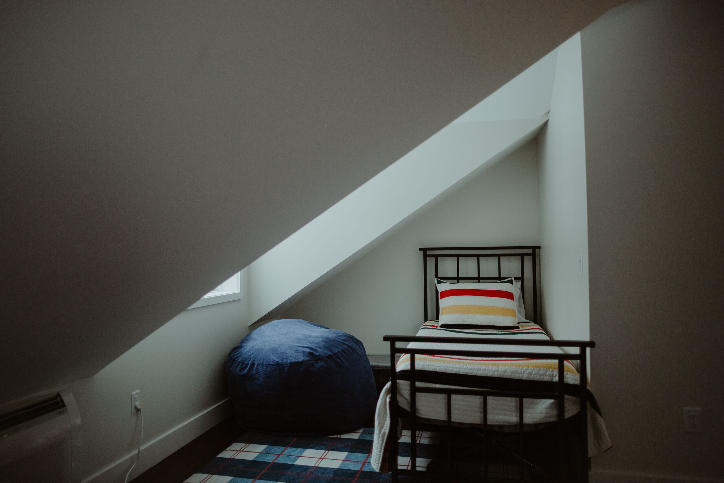 Un dormitorio estilo ático pequeño, con poca luz, que tiene una cama individual y un sillón de peluche.