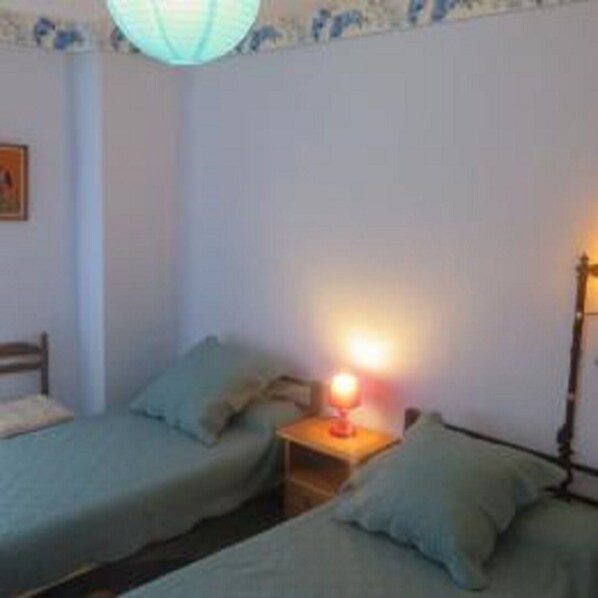 Une chambre avec deux lits simples, une table de chevet avec une lampe et une étagère fixée au mur.