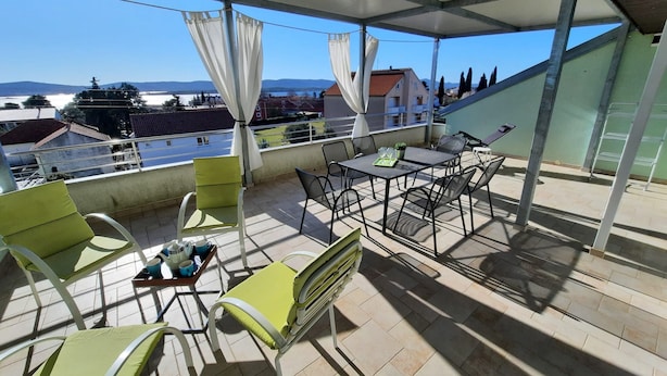 A covered terrace with outdoor furniture, a table, and a view of the surrounding area.
