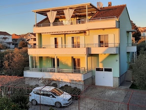A two-story residential building with balconies, large windows, and a car parked in front.