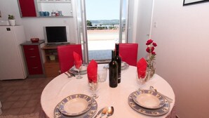 A dining table set with plates, cutlery, and wine bottles, with a view of the sea through a glass door.
