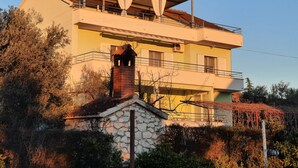 A two-story building with a flat roof, a stone foundation, and a balcony with a metal railing.