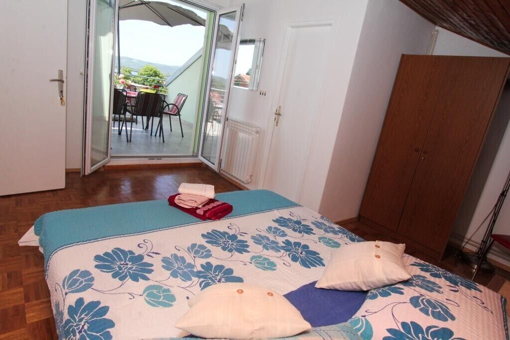 Un dormitorio con cama, armario de madera y puerta corrediza de vidrio que da a un balcón con mobiliario exterior.