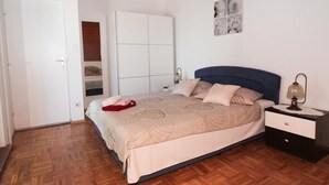 A bedroom with a bed, a nightstand, a wardrobe, and a wall with artwork.