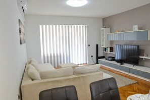 Een moderne woonkamer met een bank, stoelen, een televisie en een boekenkast.