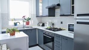 Eine moderne Küche mit grauen Schränken, einem Edelstahlkühlschrank, einem Einbauofen und einem Fenster mit Topfpflanzen.