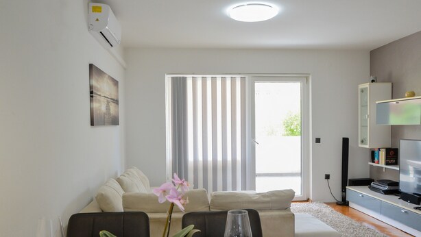 Ein modernes Wohnzimmer mit Essbereich, einer Couch, einem Fernseher und einem großen Fenster mit Jalousien.