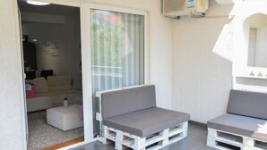 Ein Balkon mit zwei weißen Holzbänken und einer Glasschiebetür zu einem Innenraum mit einer Couch und einem Tisch.