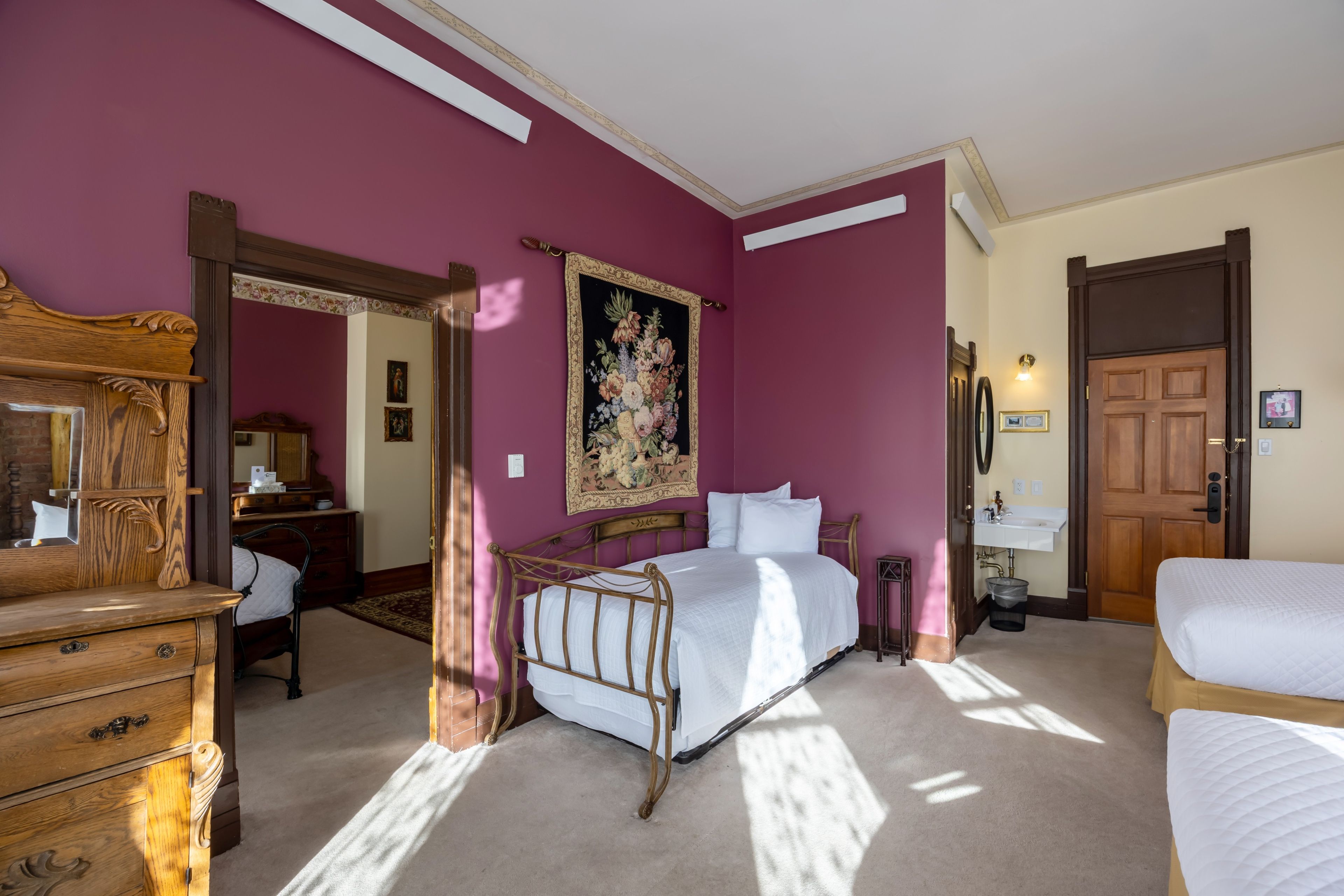 A bedroom with a bed, dresser, mirror, and a door leading to another room.