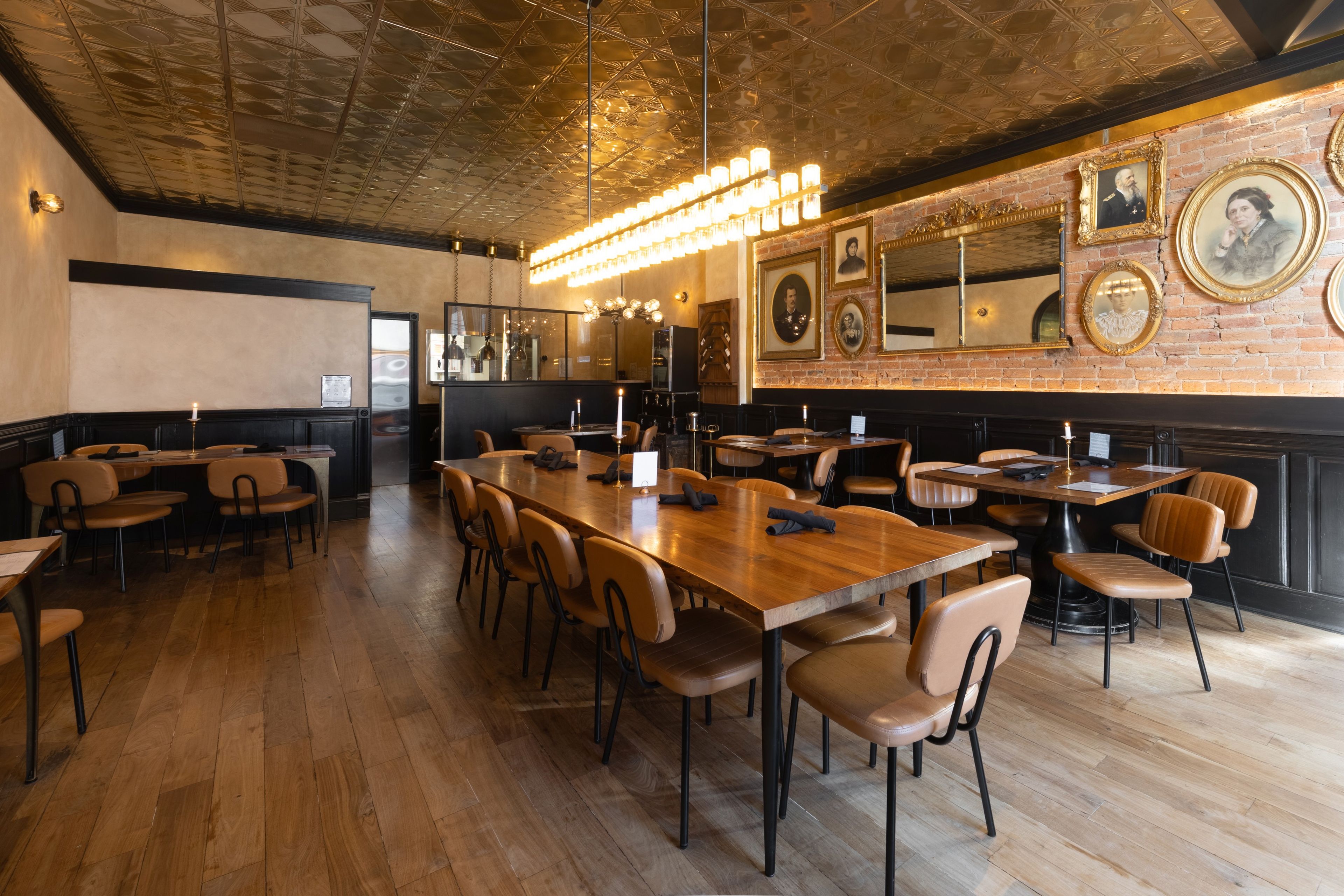 Un ristorante con un lungo tavolo in legno e numerose sedie, una parete in mattoni con ritratti incorniciati e un soffitto con motivo geometrico.