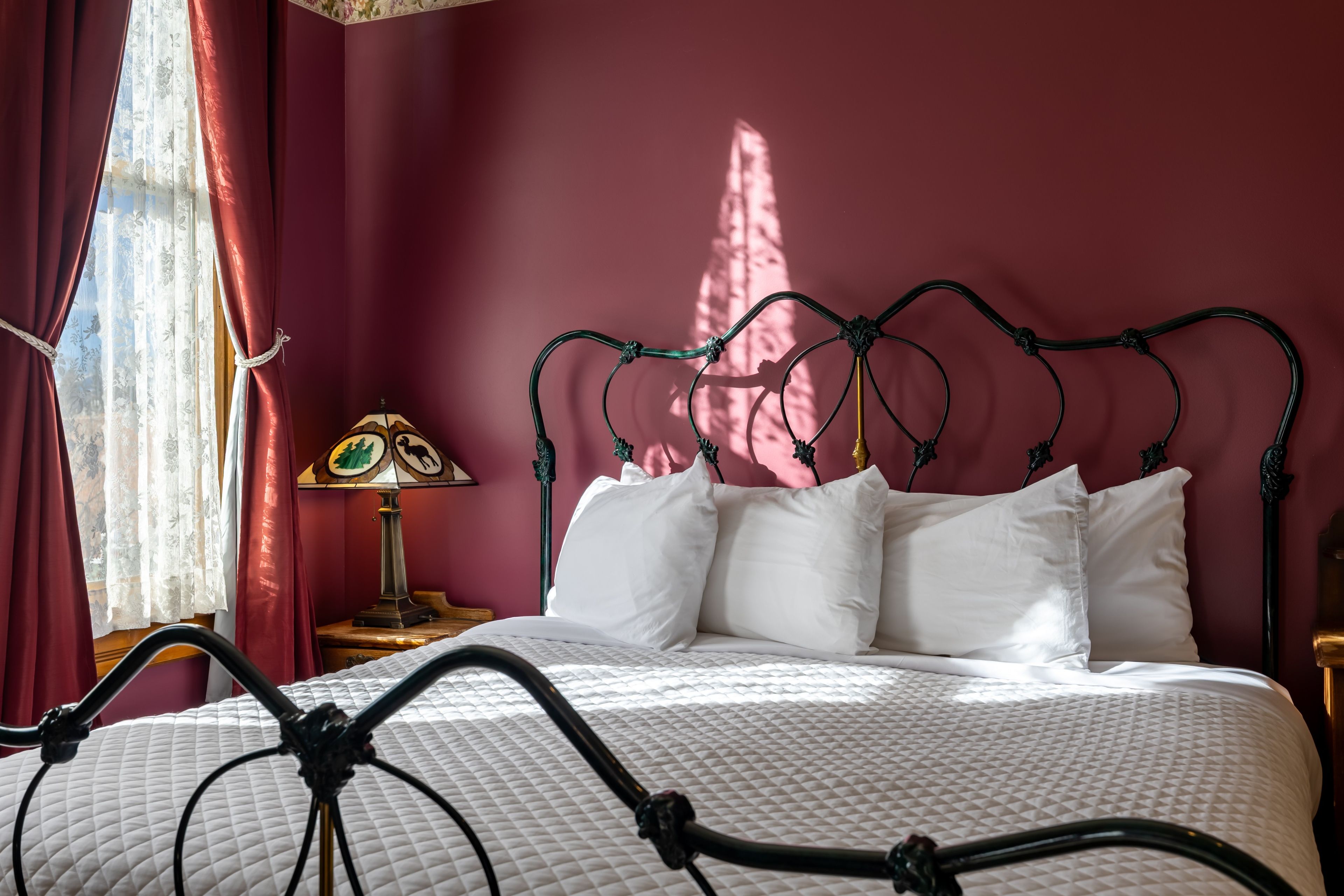 En seng med metalstel, hvide sengetøj og en lampe med blomstermønster på et natbord.