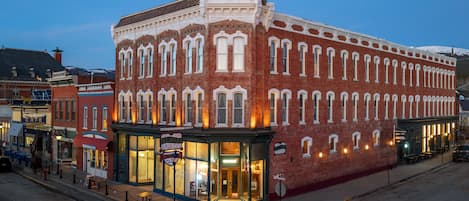 A historic red brick building with a corner entrance, a visible storefront, and a street-level seating area.