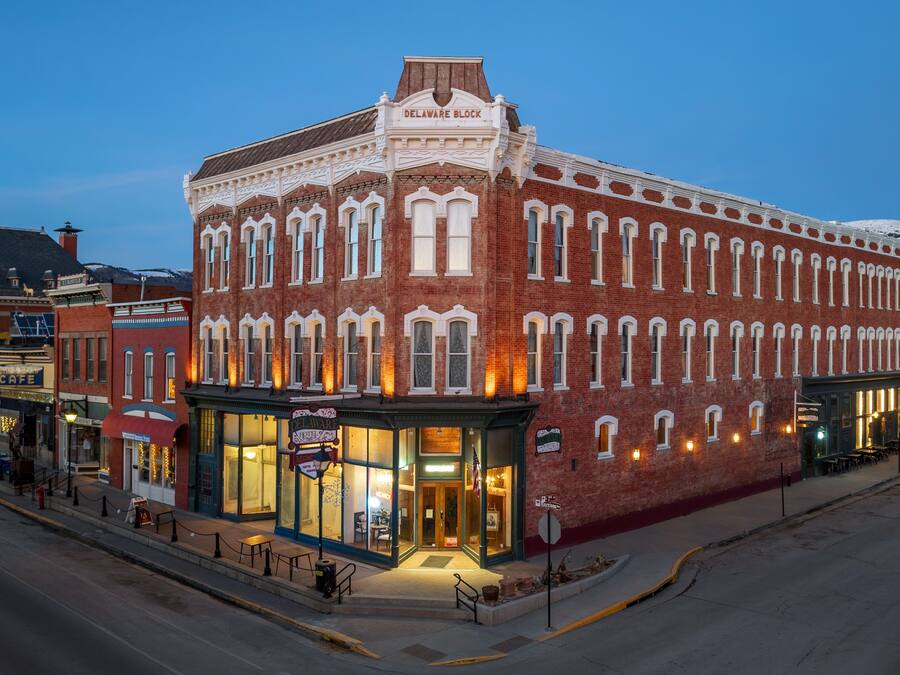 A historic red brick building with a corner entrance, a visible storefront, and a street-level seating area.