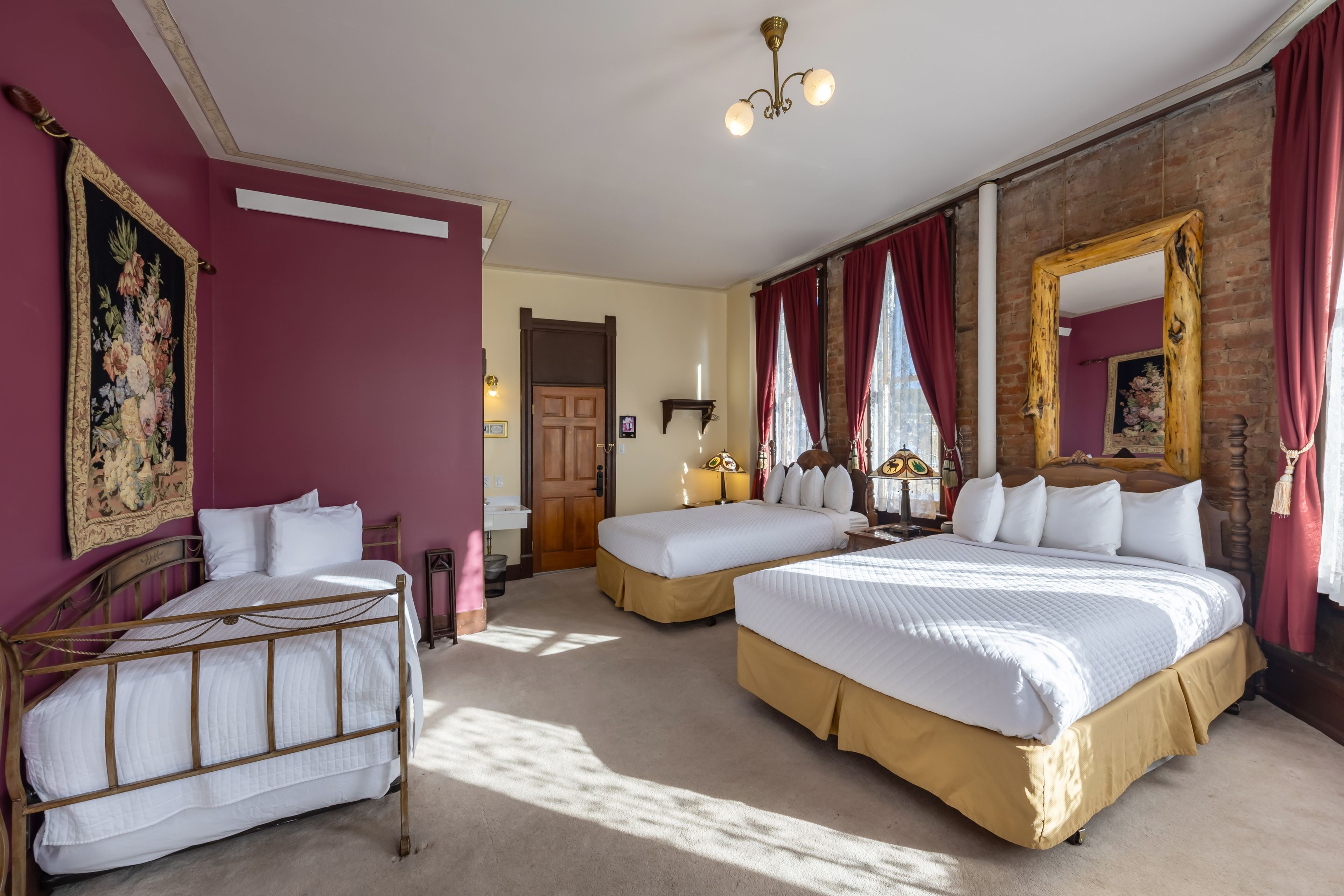 Quarto de hotel com duas camas, um espelho grande, cabeceira de madeira e cortina vermelha.