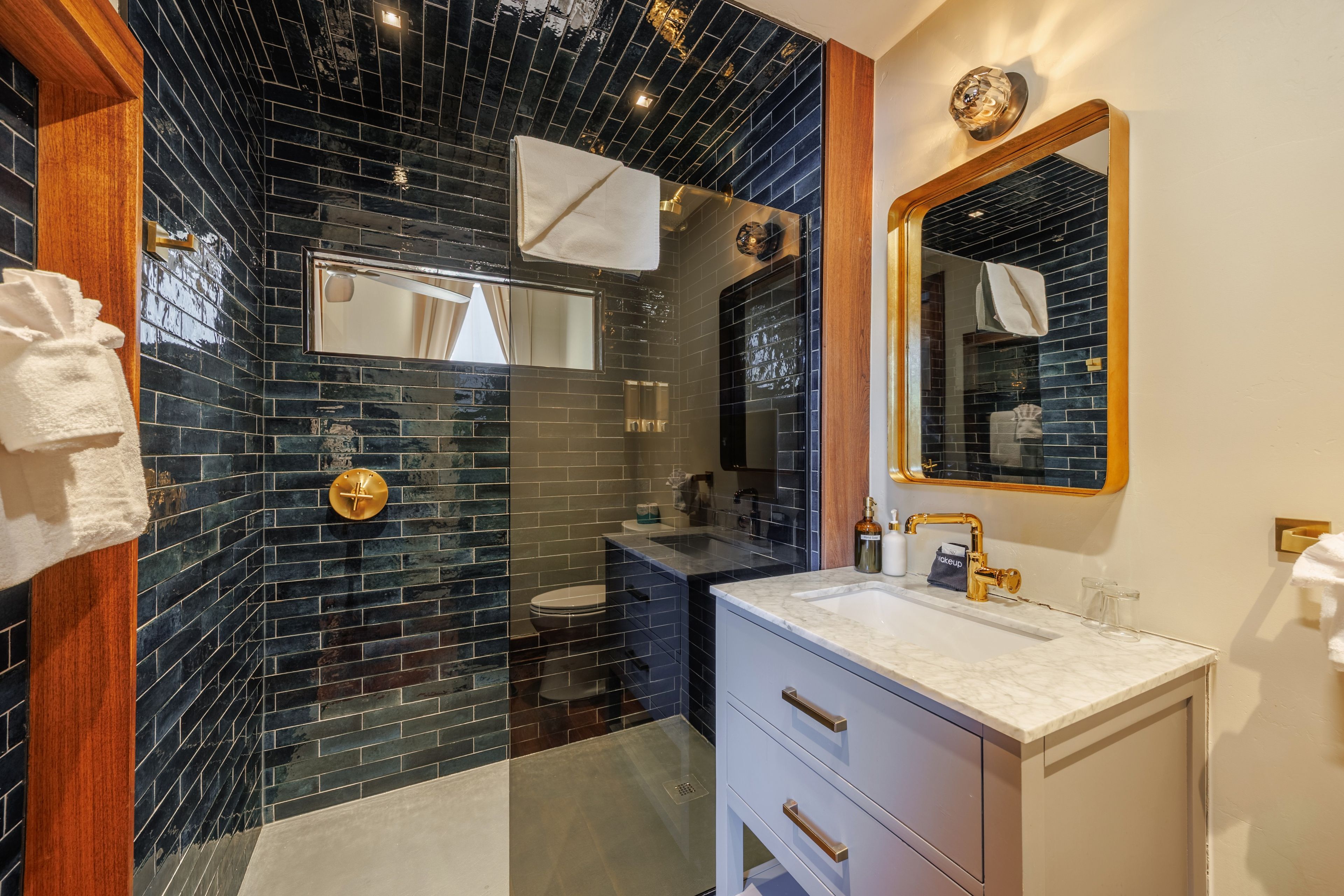 A modern bathroom with black tiled walls, a white vanity, and a gold faucet.