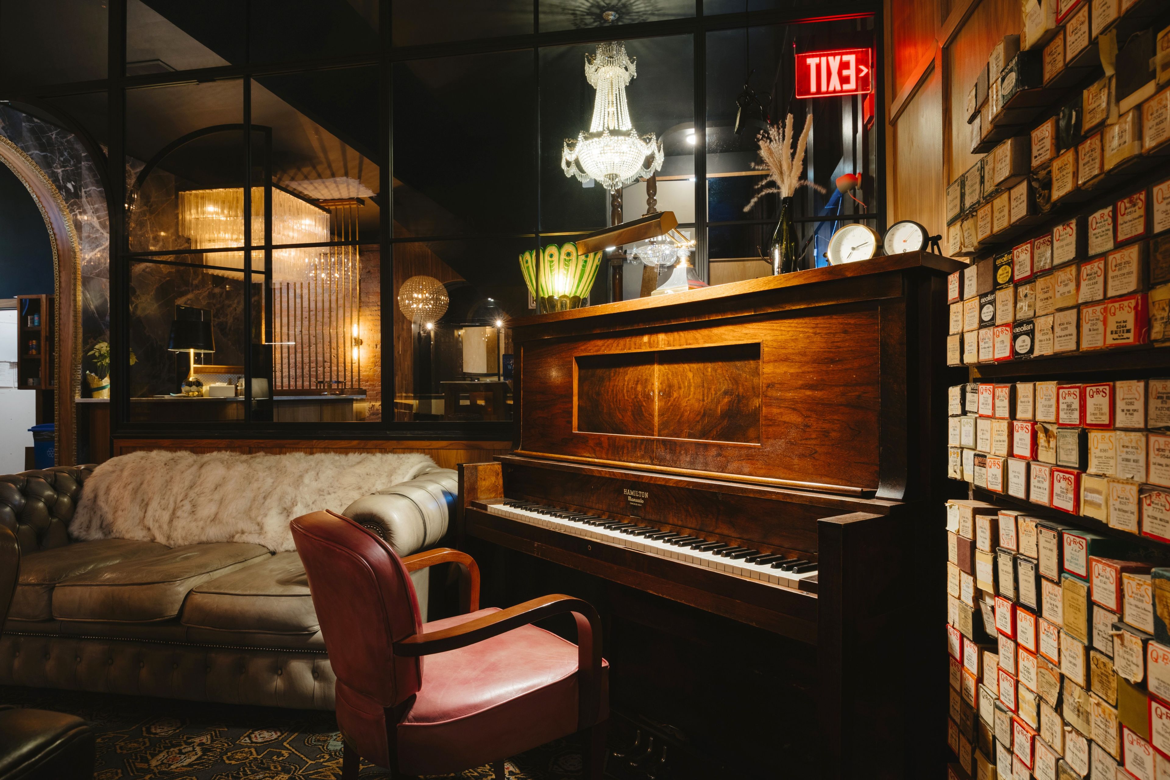 A room with a grand piano, a plush sofa, and a wall of vintage postcards.