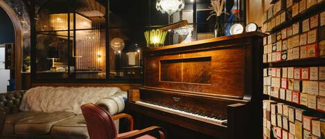 Una habitación con un piano de cola, un sofá lujoso y una pared llena de postales antiguas.