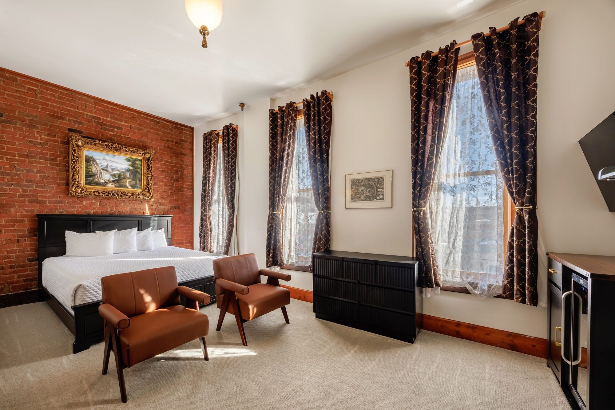 Une chambre d’hôtel avec un lit, deux chaises, un bureau, un radiateur et un téléviseur.