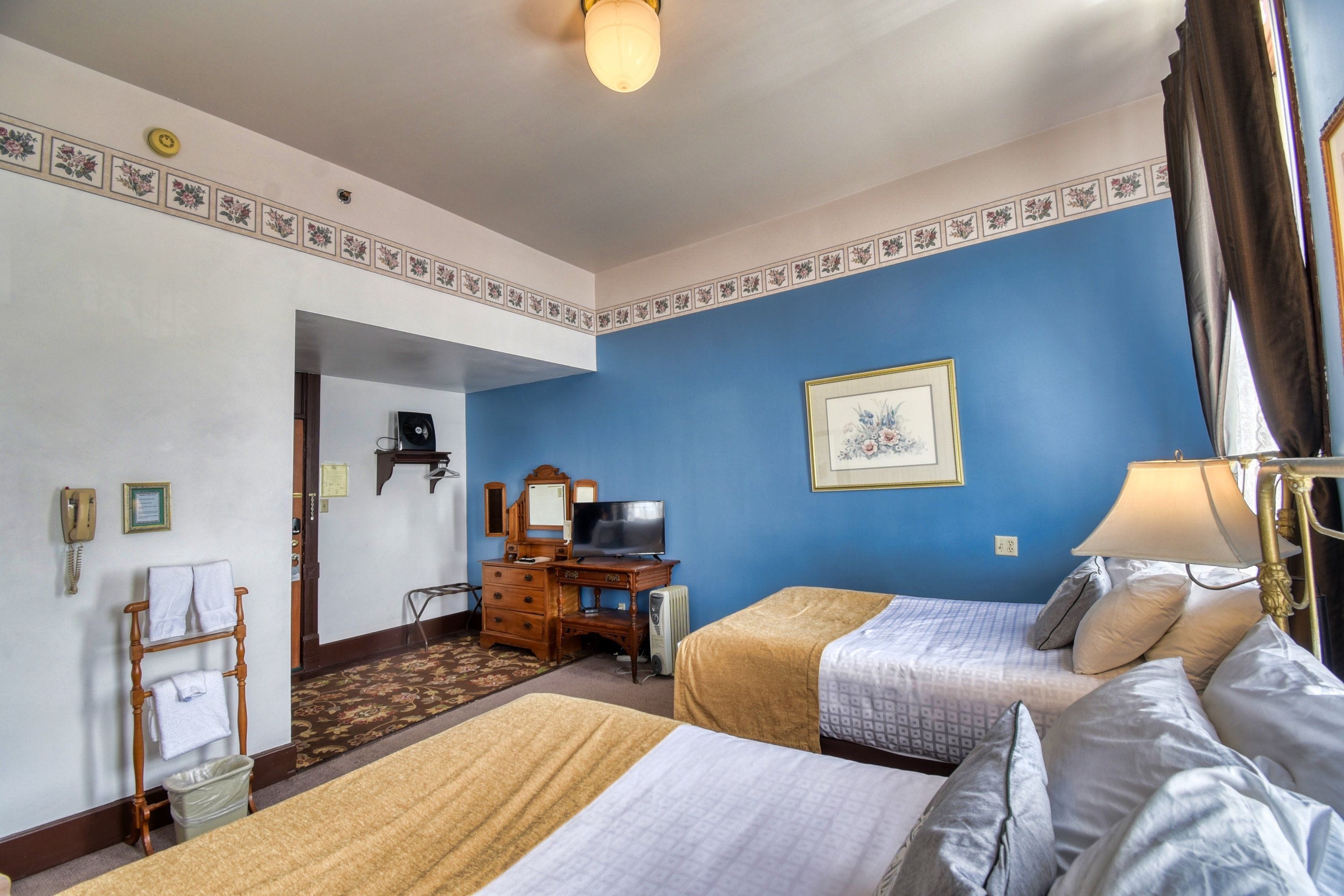 Quarto de hotel com duas camas, uma escrivaninha, televisão, telefone e espelho.