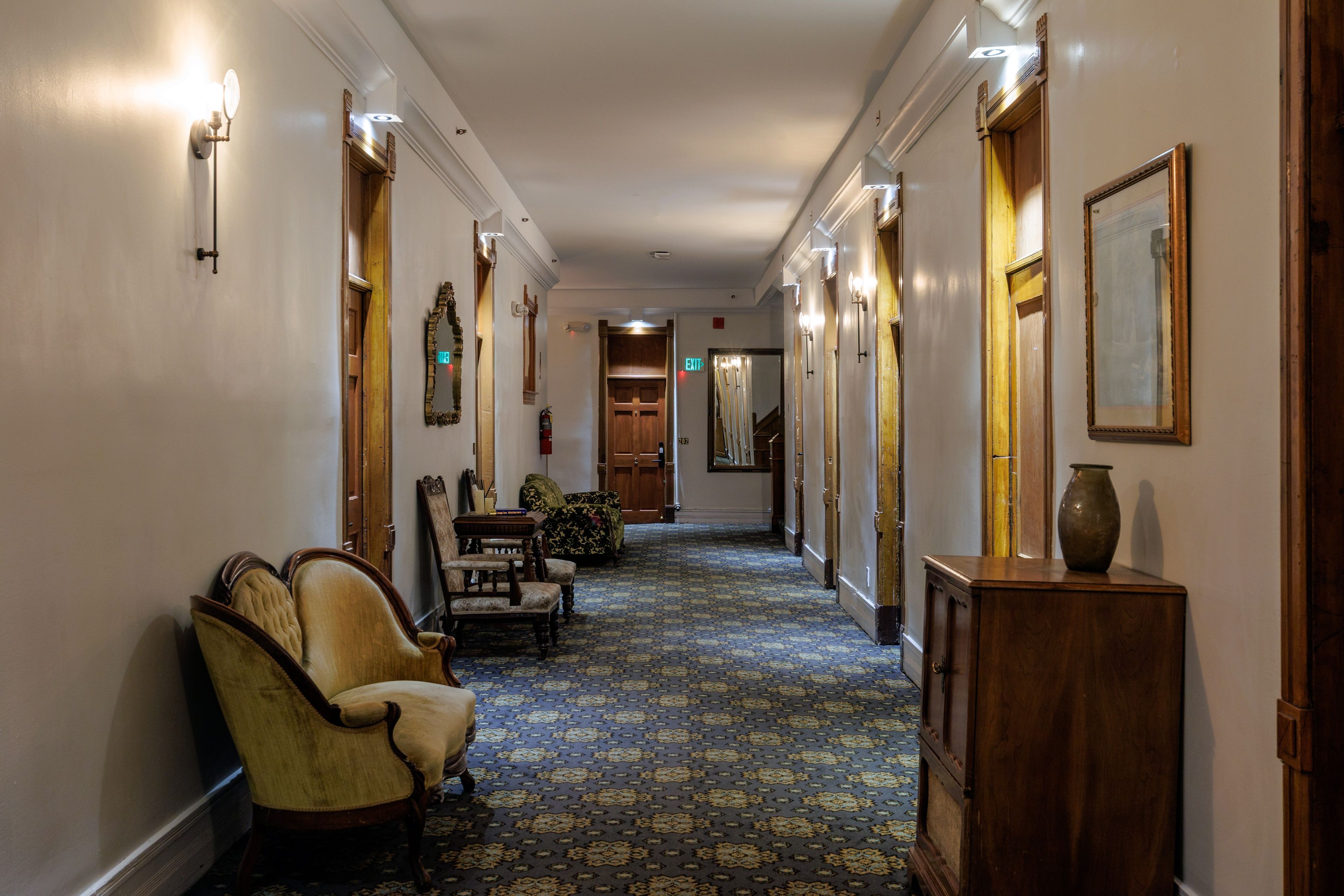 A hallway with patterned carpet, wooden doors, and traditional furniture.