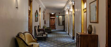 A hallway with patterned carpet, wooden doors, and traditional furniture.