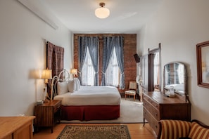 A hotel room with a large bed, a wooden nightstand, a dresser, a chair, and a mirror.