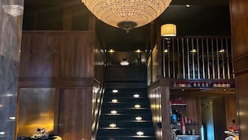 Una escalera con un candelabro, paredes de madera y una zona de bar con un letrero que dice 'DRAZBU'.