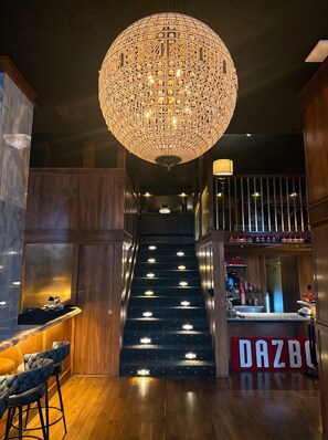 Una escalera con un candelabro, paredes de madera y una zona de bar con un letrero que dice 'DRAZBU'.