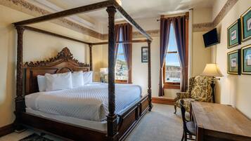 A four-poster bed with a wooden headboard, a small table, a chair, and a television mounted on the wall.