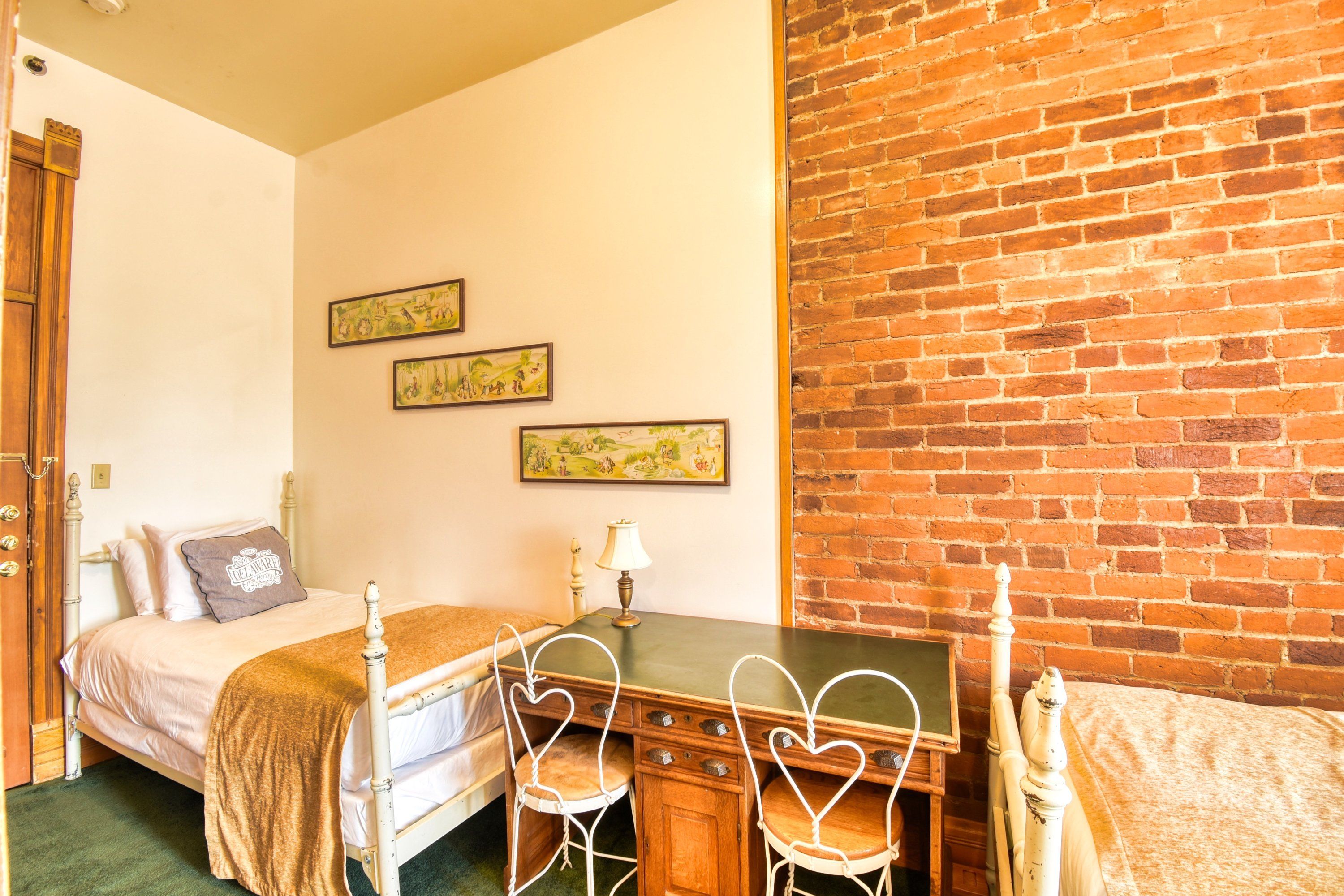 Una habitación con una cama, un escritorio y sillas con forma de corazón, junto a una pared de ladrillo.