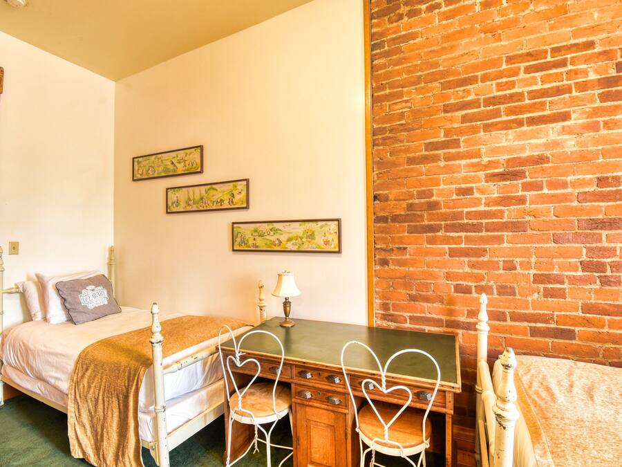 Una habitación con una cama, un escritorio y sillas con forma de corazón, junto a una pared de ladrillo.