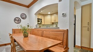 A dining area with a wooden table and benches, a potted plant, and a kitchen in the background. - Family Getaway ,Pool, Tubing, Skiing, & Ice Castles Villa 1002 (Midway)