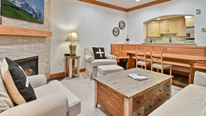 A modern living room with a fireplace, a dining area, and a kitchen with wooden cabinets and a large window. - Family Getaway ,Pool, Tubing, Skiing, & Ice Castles Villa 1002 (Midway)
