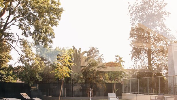 Ein rechteckiger Swimmingpool mit Holzterrasse, umgeben von Bäumen und einer Glaseinfassung.