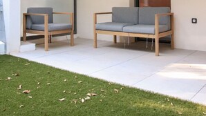 Ein moderner Außenbereich mit zwei grauen Sofas und Holzstühlen, einer Glaswand und einer hängenden Leuchte.