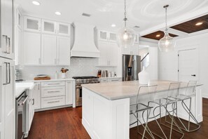 Una cocina moderna con armarios blancos, una isla central con taburetes de bar, electrodomésticos de acero inoxidable y techo de madera.