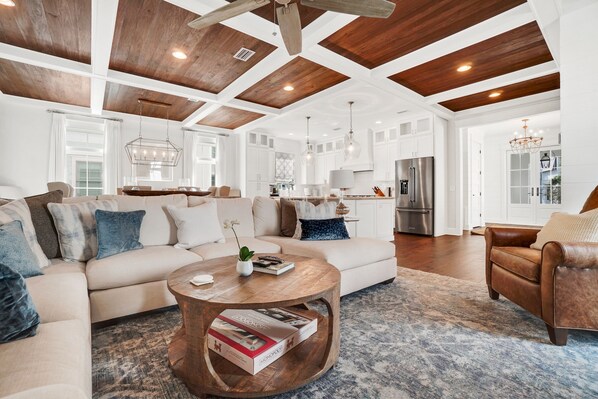 A spacious living room with a large sectional sofa, a wooden coffee table, and a chandelier. - 213 Sandyshore - Carillon Lux Home, Guest Cottage, Beach Service, Steps to Beach (Panama City Beach)