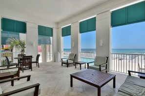 A spacious balcony with a view of the ocean, furnished with wooden chairs and tables, and large windows with green shutters. - 213 Sandyshore - Carillon Lux Home, Guest Cottage, Beach Service, Steps to Beach (Panama City Beach)
