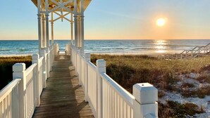 A wooden boardwalk leading to a white gazebo with a view of the ocean at sunset.