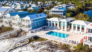 A coastal residential area with multiple houses featuring blue and white exteriors, a central swimming pool, and a wooden deck with lounge chairs.