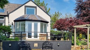A house with a bay window, a stone wall, and a garden with a pergola. - 2 bedroom accommodation in Beacon Cottage (Beacon Cottage)