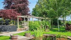 A garden with a pond, wooden pergola, and seating area. - 2 bedroom accommodation in Beacon Cottage (Beacon Cottage)