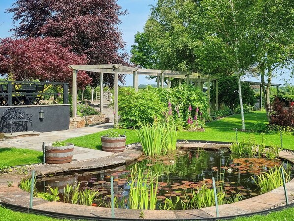 Un jardín con estanque, pérgola de madera y zona de estar.