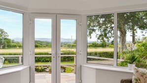 A corner room with a view of a garden, a white door, and a wicker sofa. - 2 bedroom accommodation in Beacon Cottage (Beacon Cottage)