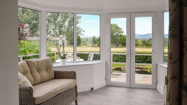 A room with a wicker sofa, large windows, and a view of a garden. - 2 bedroom accommodation in Beacon Cottage (Beacon Cottage)