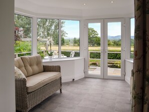 Una habitación con un sofá de mimbre, ventanas amplias y vista a un jardín.